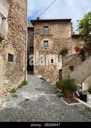 Narrow cobblestone street winding through medieval Calascio village, featuring rustic stone houses, ornate windows, colorful terracotta planters nestl Stock Photo