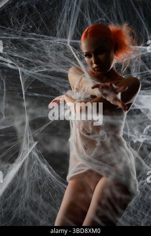 Red-haired woman is caught in a net trap surrounded by webbing at dusk Stock Photo