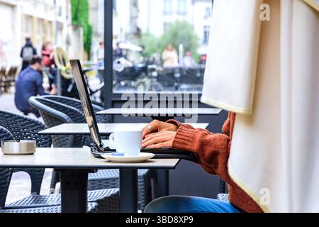 Anonymous young woman working on a lap-top computer at an outdoor cafe table - Tours, Indre-et-Loire (37), France. Stock Photo