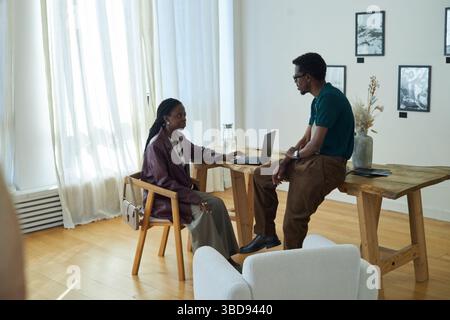 Two coworkers engaged in discussion at wooden table in contemporary art gallery Stock Photo