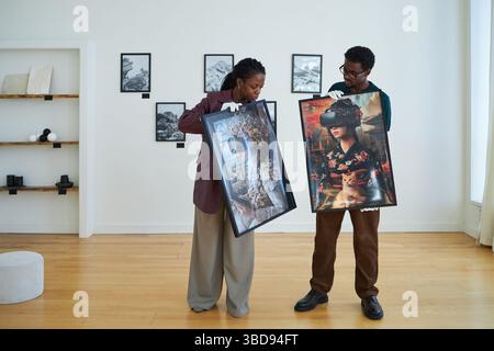 Two people viewing large framed artworks in contemporary gallery space featuring minimalist decor and wooden flooring. Engaging with the pieces in rel Stock Photo