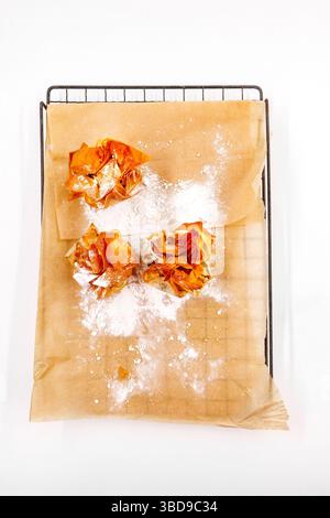 Three baked pastries dusted with powdered sugar on parchment paper over a metal cooling rack Stock Photo