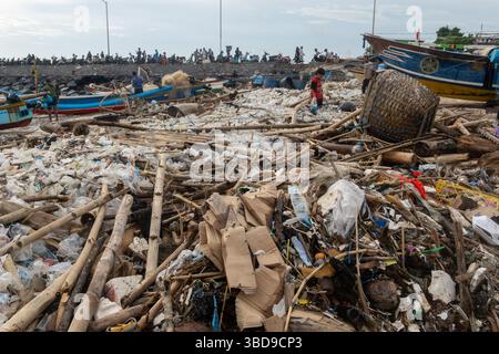 Bali, Indonesia - Dec 22, 2024: Beach is covered in trash and debris. The scene is chaotic and disorganized, with people scattered around the area. Sc Stock Photo