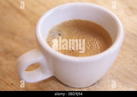 Freshly brewed espresso in a classic white cup on a rustic wooden surface. Rich crema highlights texture and quality, ideal for coffee-themed stock im Stock Photo