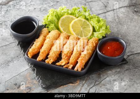 Tempura deep-fried EBI prawns with spiced sauces closeup on plate on the table. Horizontal Stock Photo