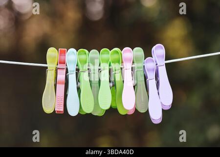 Colorful plastic clothespins on rope. Hanging clips outdoors. Laundry concept in daylight. Bright household detail. Multicolor peg arrangement. Stock Photo