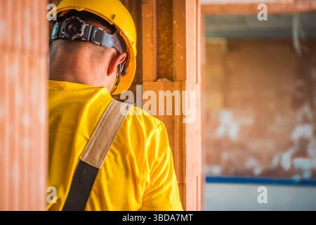 A construction worker wearing a yellow helmet and shirt is focused on tasks within a partially constructed building. The environment shows unfinished Stock Photo