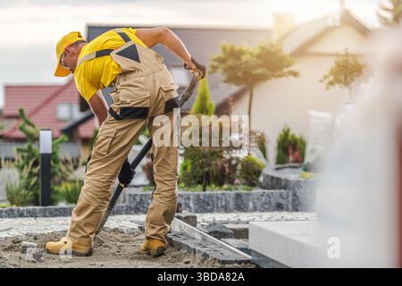 A dedicated worker in a yellow shirt and hat mixes and lays concrete in a residential landscape. The project is set in a suburban neighborhood with mo Stock Photo