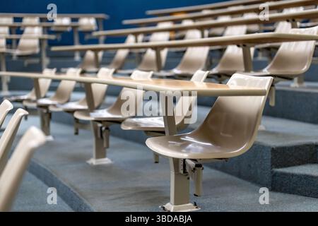 Closeup of a table and chair in an empty college or university classroom or lecture hall. Wooden desks and plastic integrated chair, no people Stock Photo