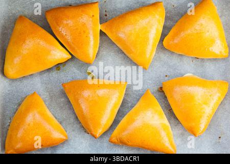 Homemade baked triangular buns lie on white parchment. Stock Photo