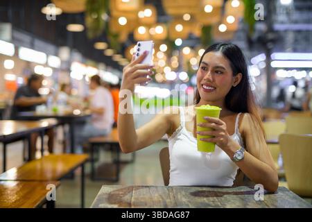 Young beautiful Asian woman drinking healthy avocado smoothie drink in cafe at night Stock Photo