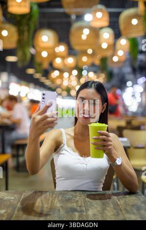 Young beautiful Asian woman drinking healthy avocado smoothie drink in cafe at night Stock Photo