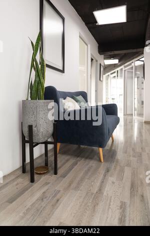 A stylish waiting room featuring a vibrant blue sofa paired with a sleek metal plant stand, creating a modern and aesthetic atmosphere for visitors. Stock Photo