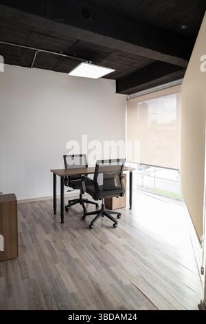 A compact glass meeting space with two black chairs and a round table, creating a sleek and modern environment for private discussions and teamwork. Stock Photo