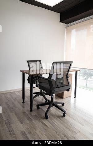 A stylish glass-enclosed meeting room featuring two black chairs and a small table, designed for professional discussions and private teamwork session Stock Photo