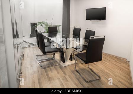 A modern meeting room featuring a transparent glass table surrounded by sleek black chairs, creating a stylish and professional environment for discus Stock Photo
