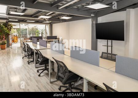 A bright and open coworking area featuring long tables and multiple chairs, designed for collaboration, productivity, and flexible work in a contempor Stock Photo