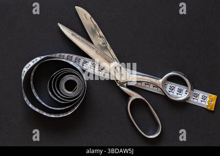 Metal dressmaker scissors and tape measure on black background, sewing and cutting tool Stock Photo