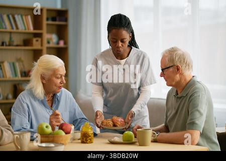Elderly Couple Having Breakfast with Caregivers Assistance Stock Photo