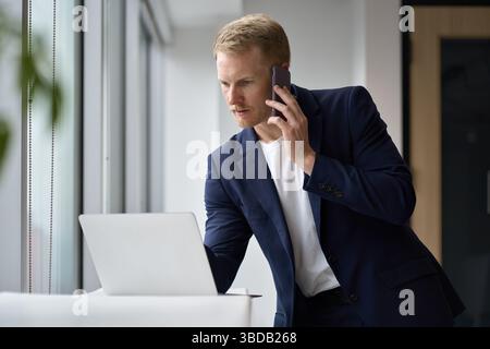 Busy professional business man using laptop talking on phone in office. Stock Photo