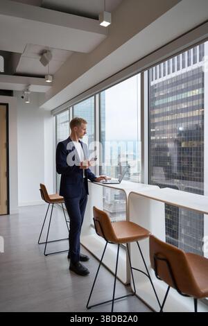 Busy young business man in office working on laptop using phone. Stock Photo