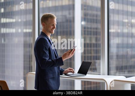 Happy business man investor looking at smartphone woking in office. Stock Photo