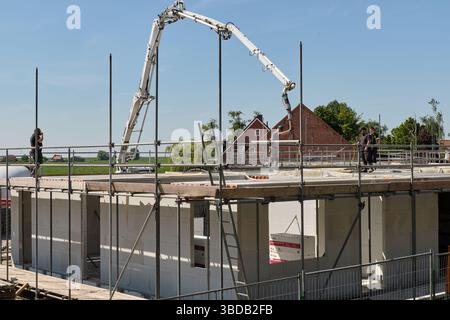 April 30, 2025 - Stavenisse-Netherlands: Workers pour concrete in a floor using a pump truck at a building site in a Dutch village surrounded by green Stock Photo