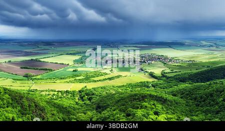 Summer storm clouds seen from a drone over a vast green forest and village with houses in a fairy tale landscape. Stock Photo