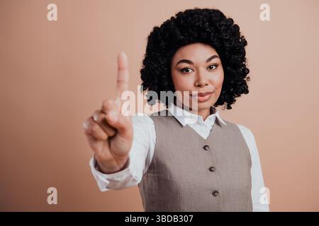 Confident businesswoman making a point with hand gesture against a beige backdrop in formal attire and professional demeanor Stock Photo