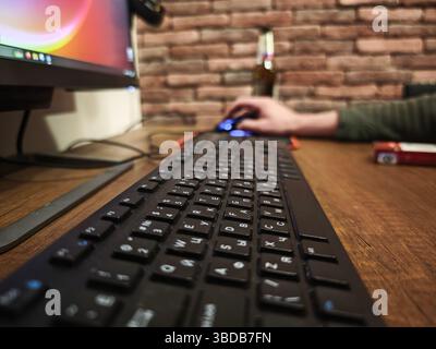Close up of a black keyboard on a wooden desk, with a programmer using a mouse and working on a computer in a home office setting Stock Photo