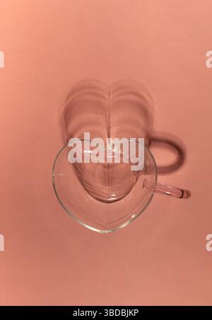 Heart shaped glass cup with shadow on pink background. Minimalist composition Stock Photo