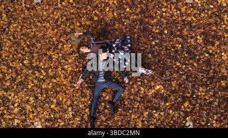 Aerial view  of an attractive young woman and man laying on the forest floor surrounded by leaves in autumn colours. Elevated photo of romantic couple Stock Photo