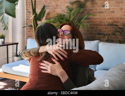 Two happy business women sitting on sofa at work in office and hugging. Stock Photo