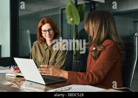 Two happy female coworkers working together using computer at desk in office. Stock Photo