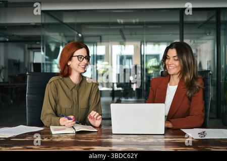 Two happy female coworkers working together using computer at desk in office. Stock Photo