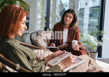 Two busy businesswomen having conversation working in green cozy office. Stock Photo
