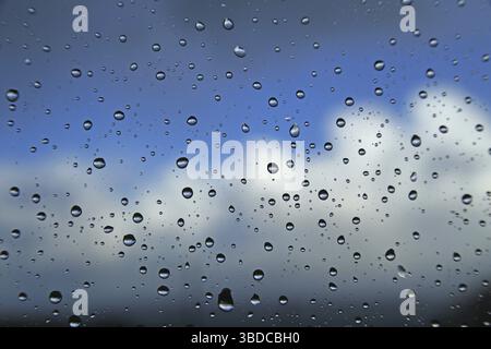 Raindrops on a window pane against a blue sky with clouds Raindrops on a window pane against a blue sky with clouds Stock Photo