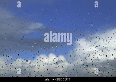 Raindrops on a window pane against a blue sky with clouds Raindrops on a window pane against a blue sky with clouds Stock Photo
