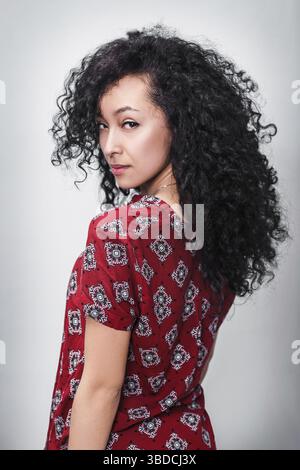 Young beautiful woman with curly black hair over gray background Stock Photo