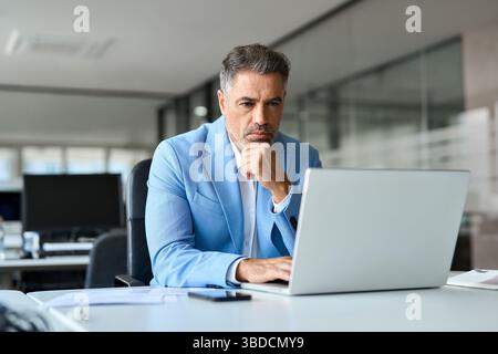 Serious busy middle aged professional business man using laptop in office. Stock Photo