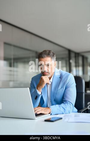 Busy middle aged professional businessman using laptop working at desk. Vertical Stock Photo