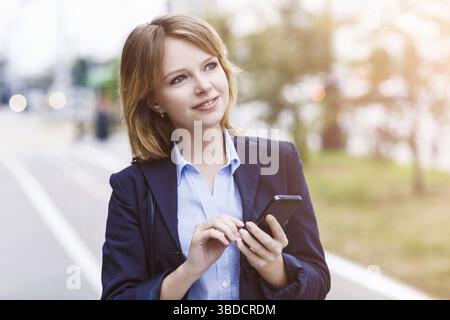 Thoughtful businesswoman sending message with smartphone outdoors Stock Photo