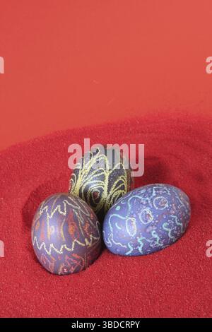 Three colourfully painted Easter eggs in a nest of red decorative gravel Stock Photo