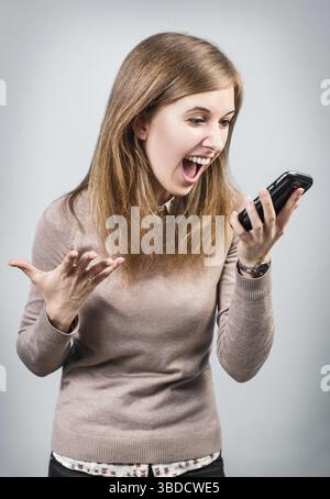 Angry businesswoman shouting on smartphone over gray background Stock Photo