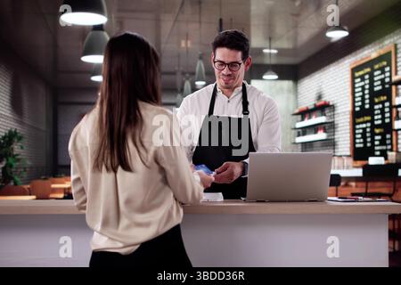 Smiling Customer Pays Barista With Credit Card In Happy Cafe Stock Photo