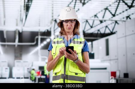 An Older Woman In An Industrial Setting Using Her Smartphone. Stock Photo