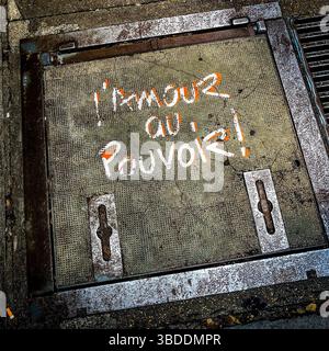 "l'amour au pouvoir" (love in power) hand-painted graffiti message on pavement hatch cover - Montmartre, Paris 75018, France. Stock Photo