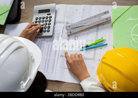 Engineers are Collaborating on Construction Plans while Utilizing Various Calculating Tools Stock Photo