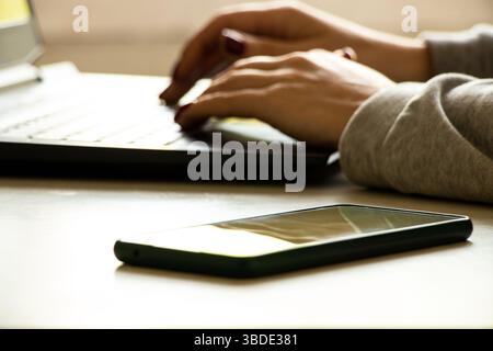 Work from home, woman with phone and laptop works in apartment, remote work and freelancing concept Stock Photo