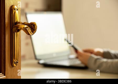 Work from home, woman with phone and laptop against open door, remote work and freelancing concept Stock Photo